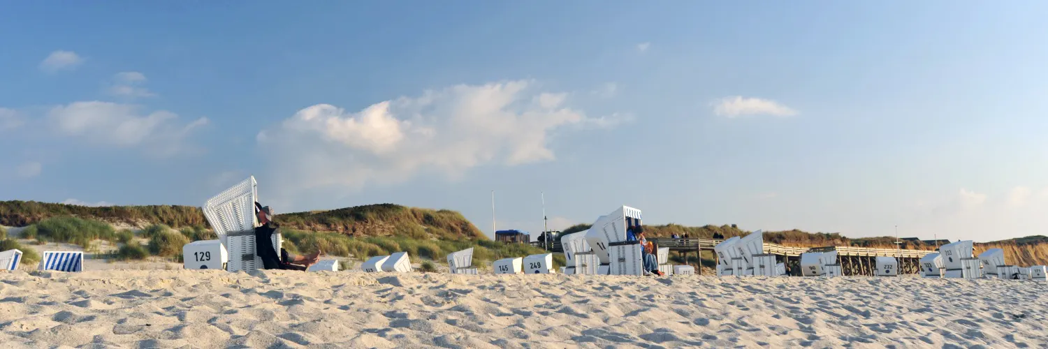 Sandstrand mit weißen Strandkörben vor den Dünen auf Sylt